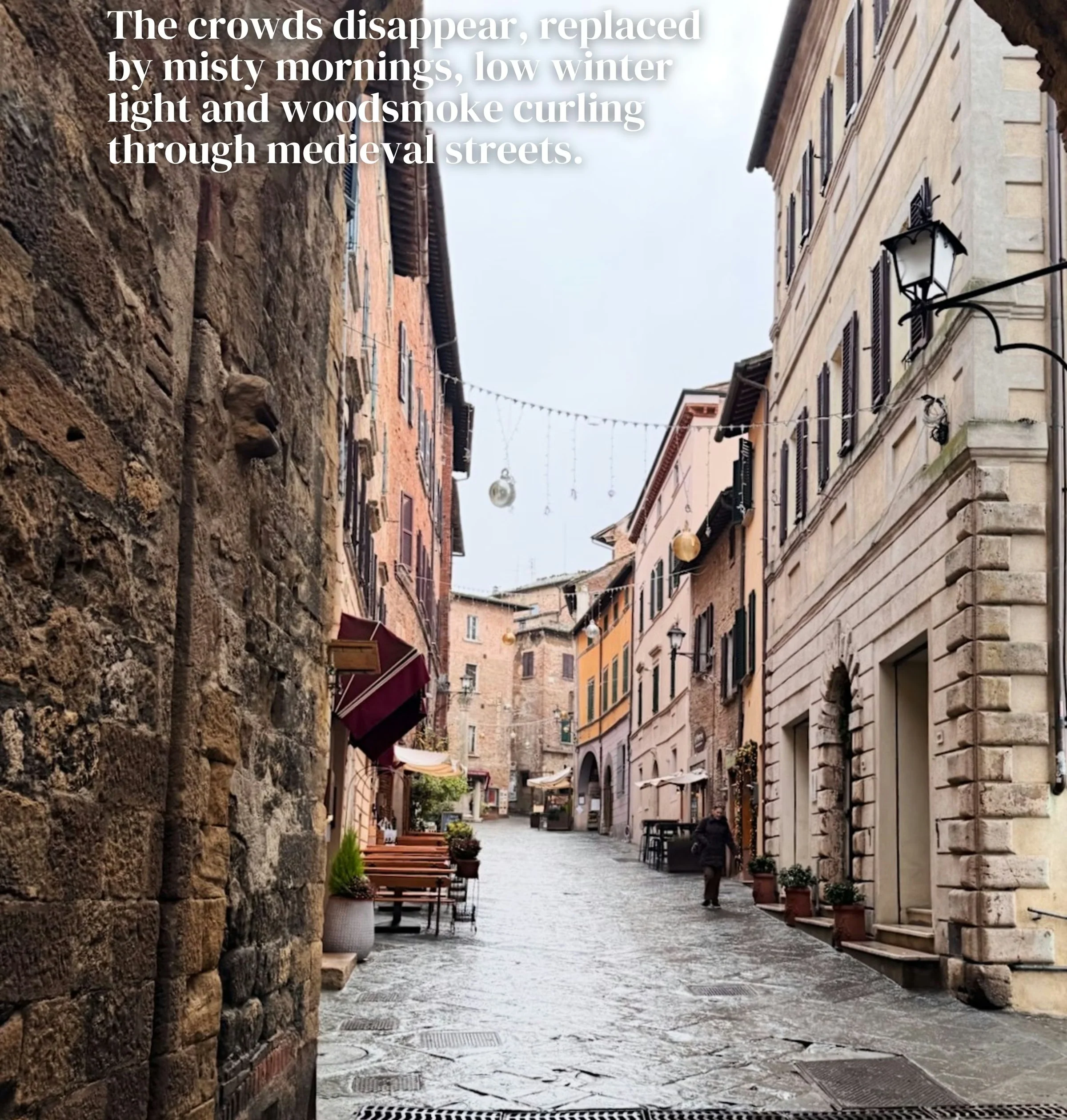 Rainy stone street in Montalcino, Tuscany, framed by a historic arch