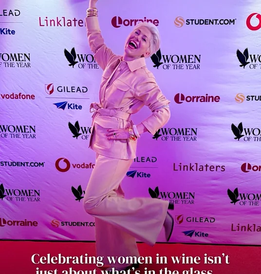 Person posing on a red carpet in front of a Women of the Year sponsor backdrop