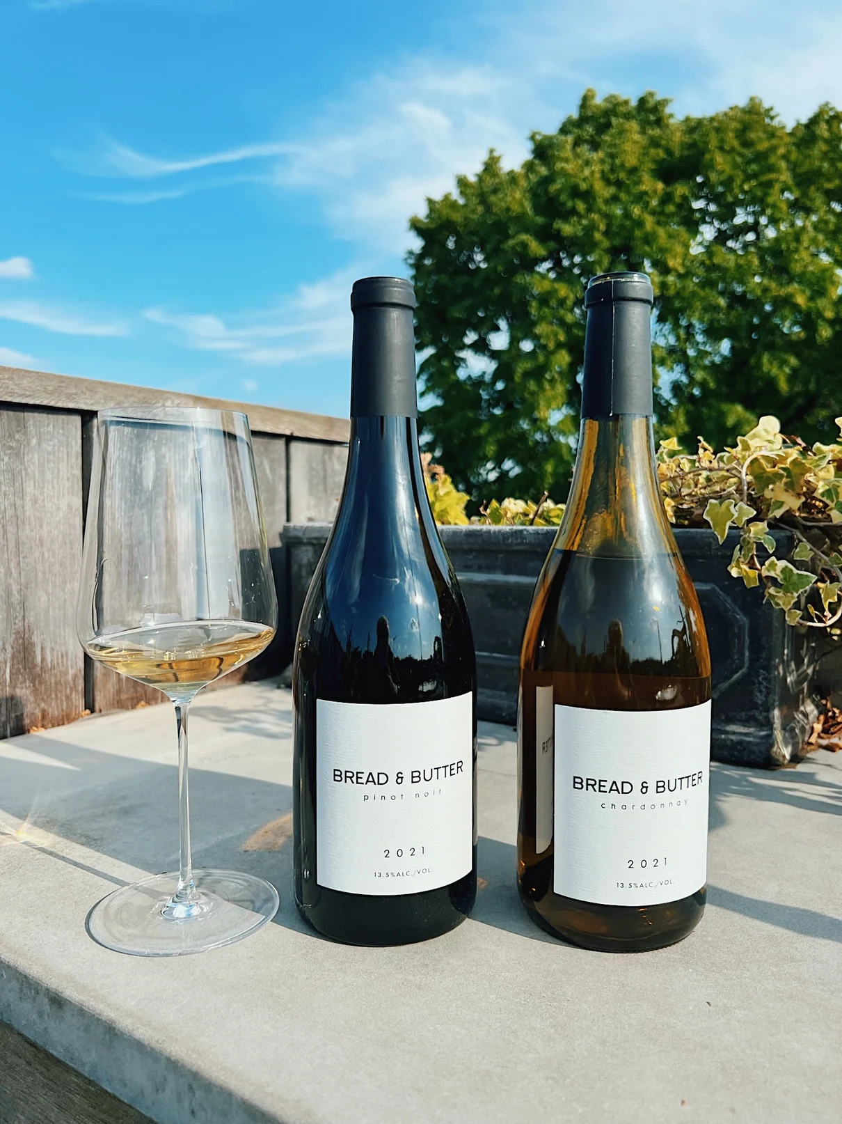 Two wine bottles and a glass on a sunny terrace
