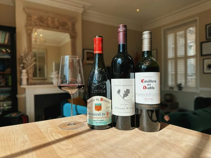 Three wine bottles and a glass on a wooden table