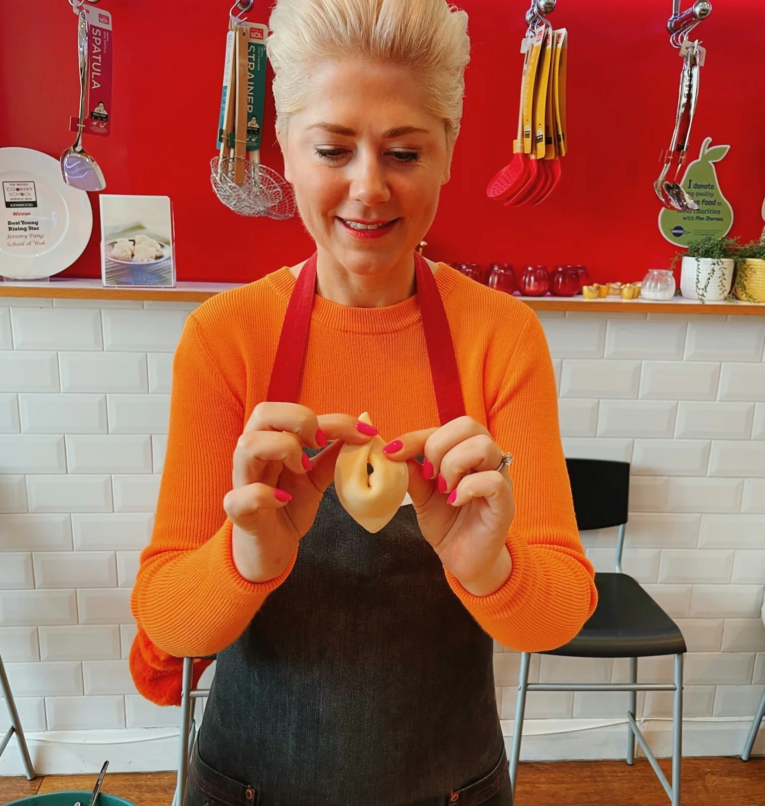 Cook in an orange jumper and apron holds a piece of food in a brightly coloured kitchen