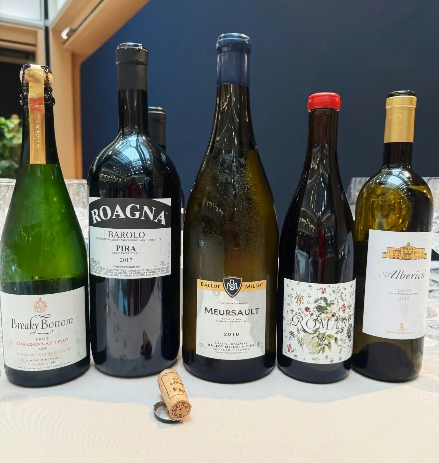 Six wine bottles, including Roagna Barolo, Meursault and Alberico, arranged on a table in an office