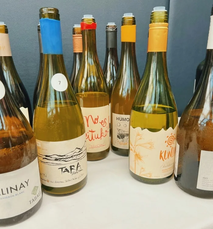 Close-up of natural wine bottles with colourful neck labels arranged on a white surface