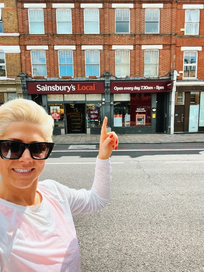 Woman pointing at Sainsbury’s Local on a London street