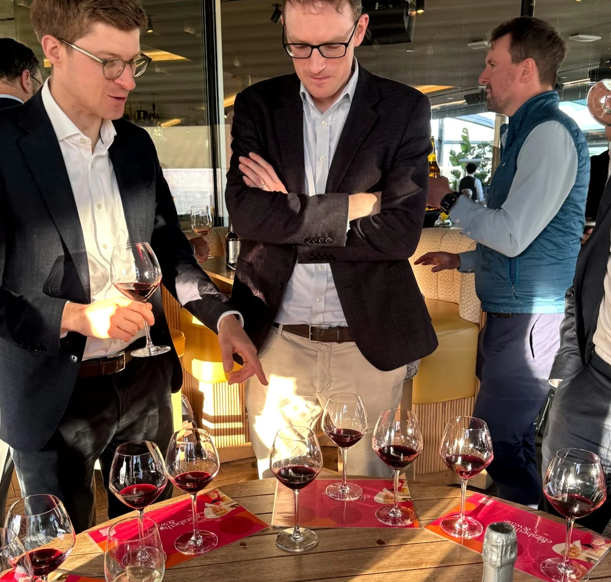 Guests mingle around a table of red wine glasses during a blind wine tasting