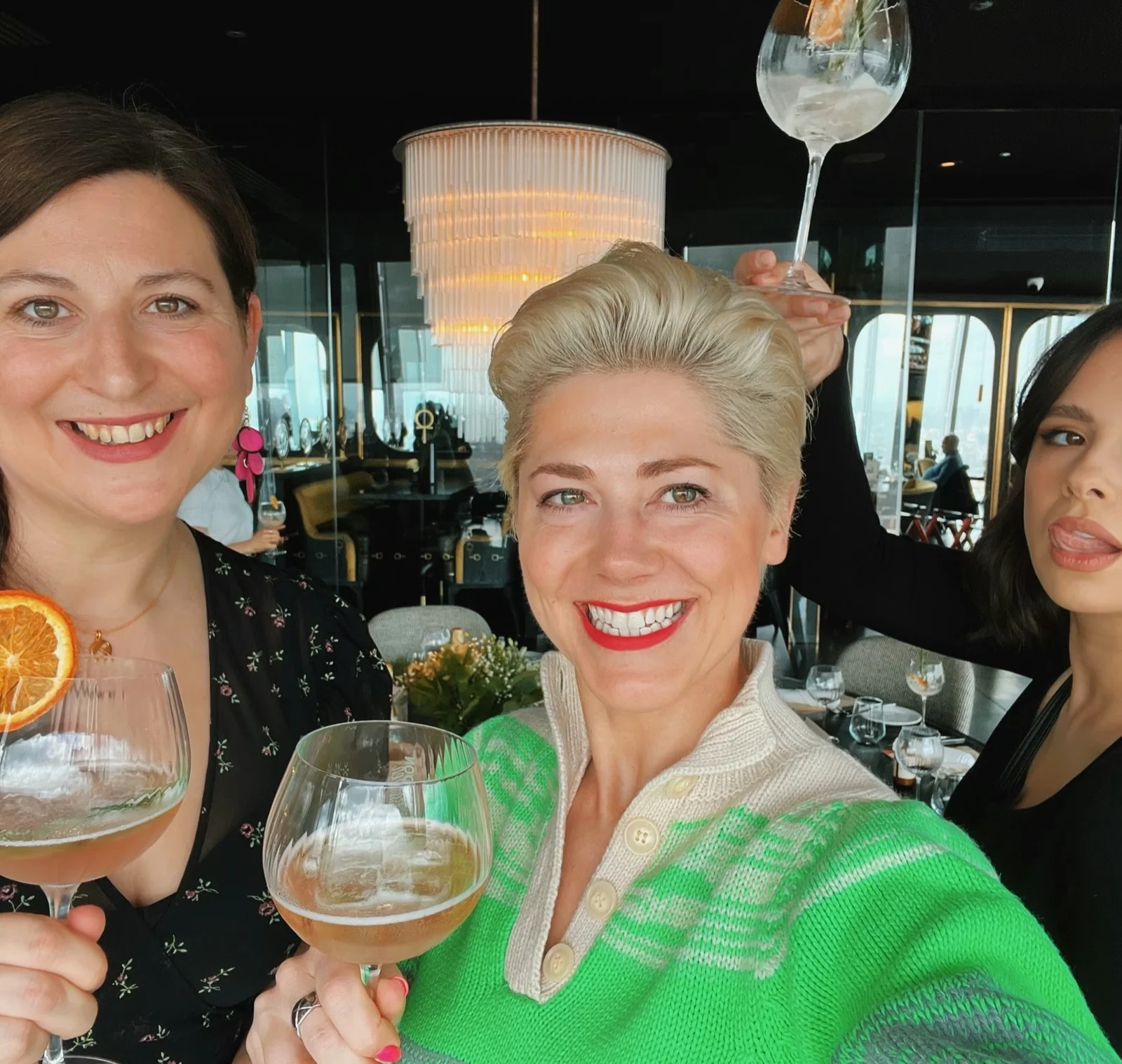Three women smile at a restaurant table while holding large wine glasses