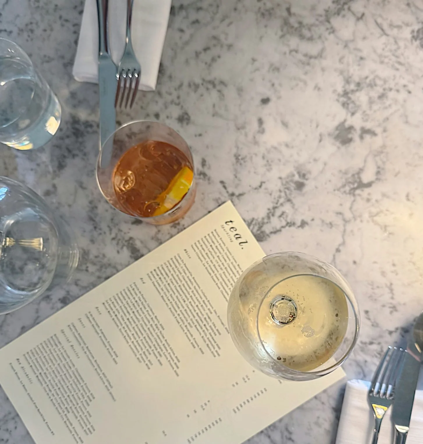 Restaurant table with two drinks, cutlery and a printed menu on a marble surface
