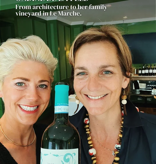 Two women smiling beside a bottle of Misco 2021 wine in a green room