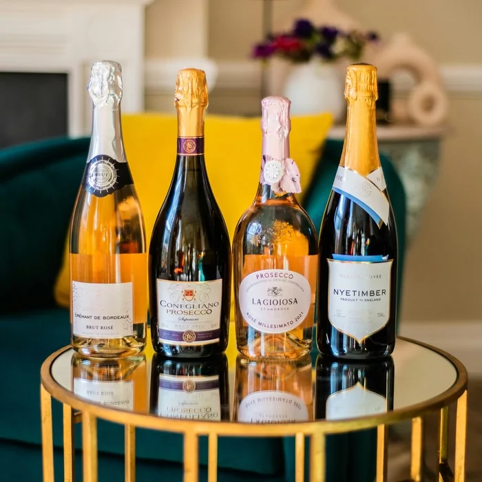 Four sparkling wine bottles on a gold table, including English Nyetimber