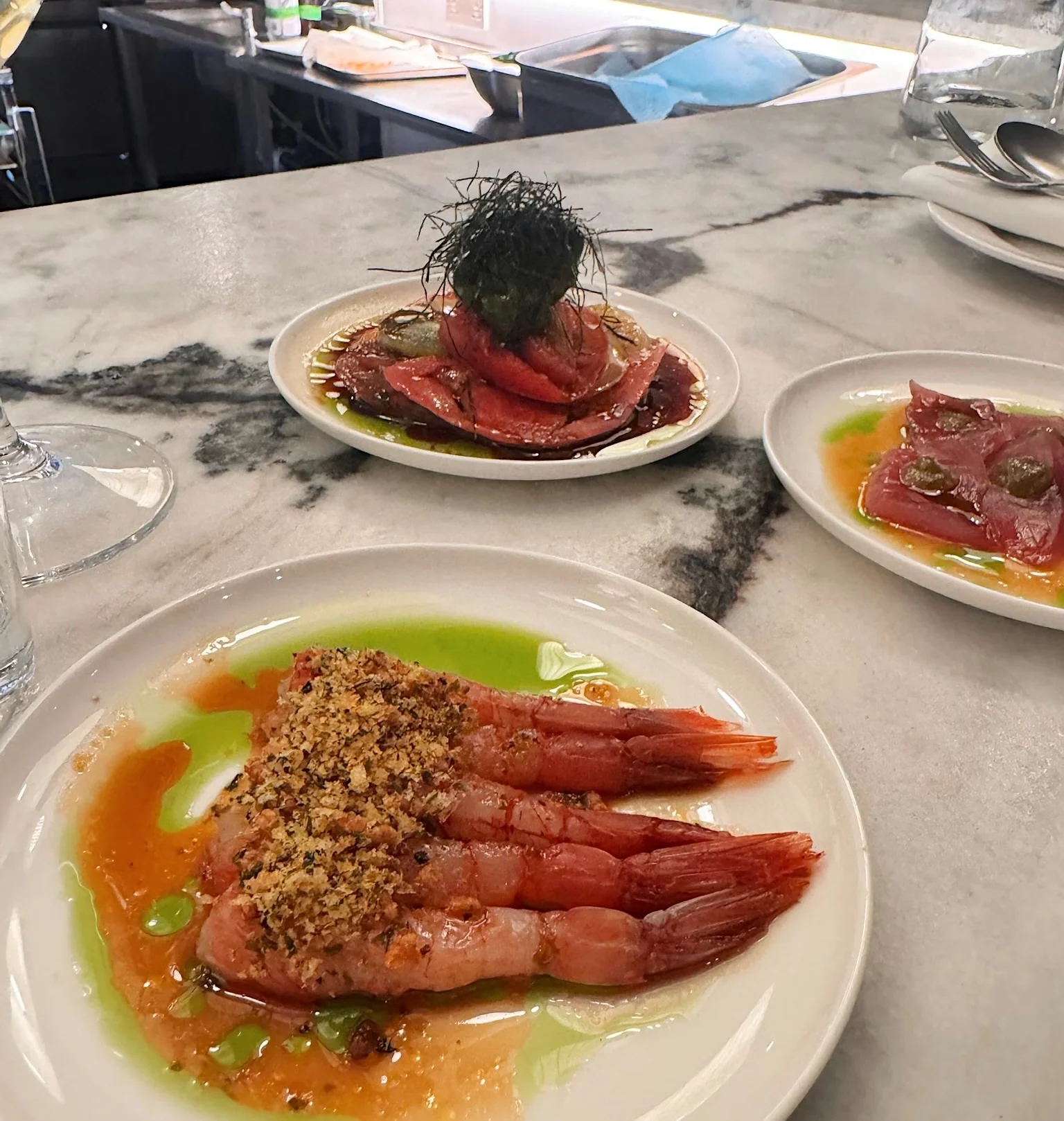 Plated prawns with crisp topping and green oil, served at a restaurant counter