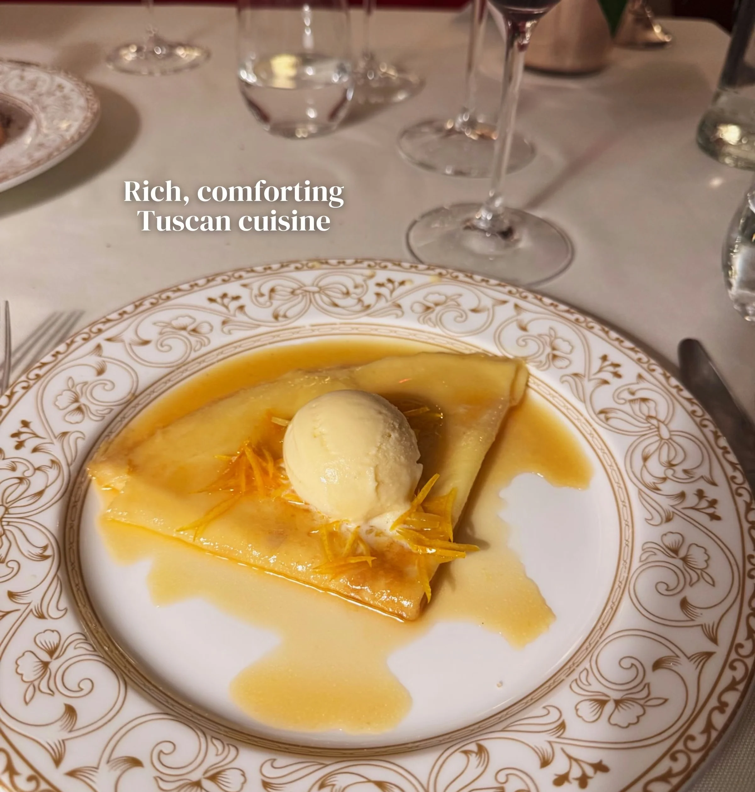 Dessert with a scoop of ice cream on an ornate plate, surrounded by wine glasses