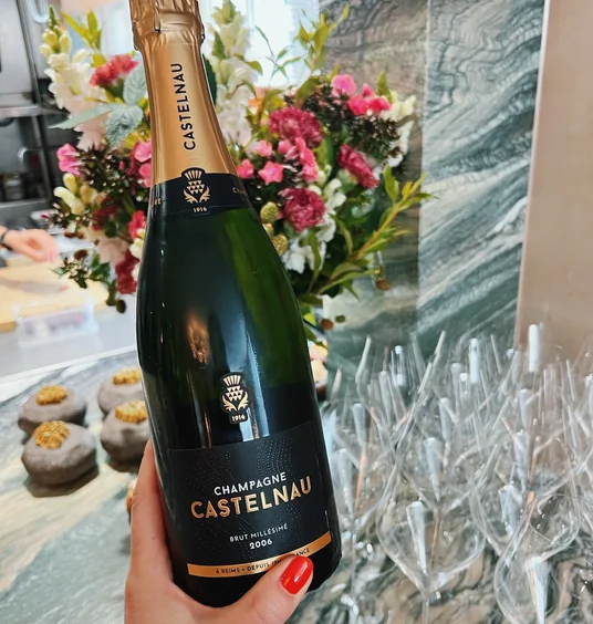 Champagne Castelnau bottle held in front of flowers and rows of wine glasses