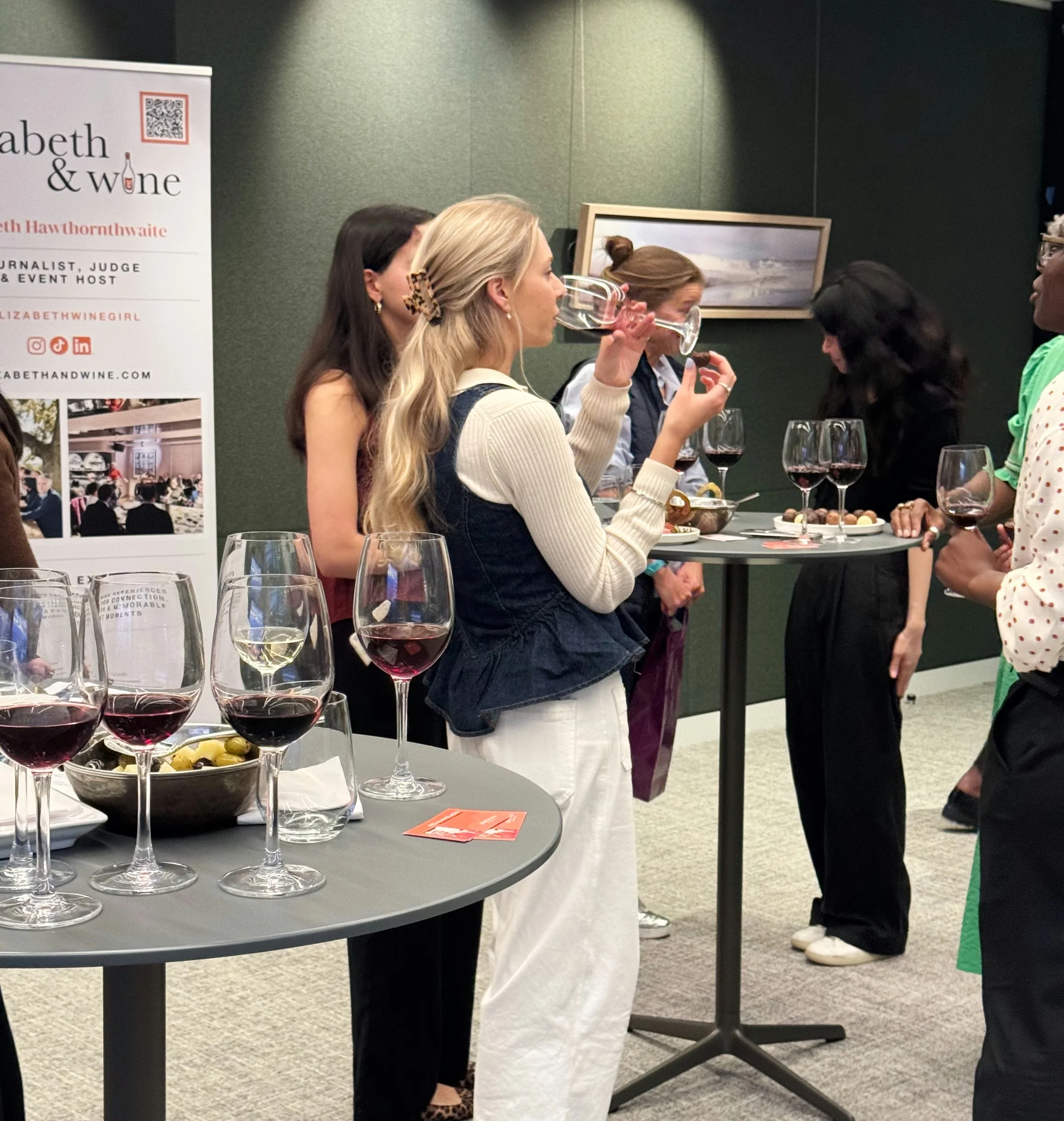 Guests mingle over wine at a networking event, with glasses and canapés on tables