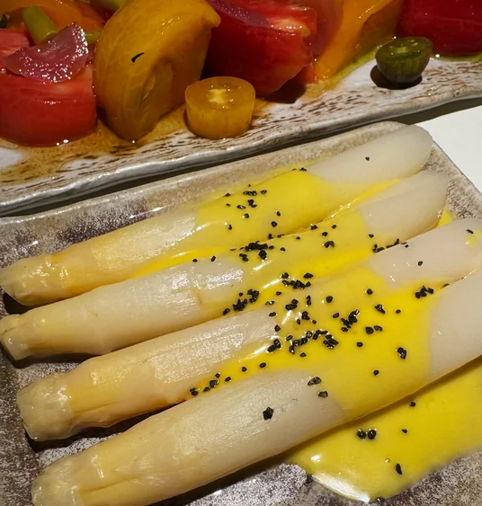 White asparagus with yellow sauce and black salt, alongside a salad of red, yellow and green tomatoes