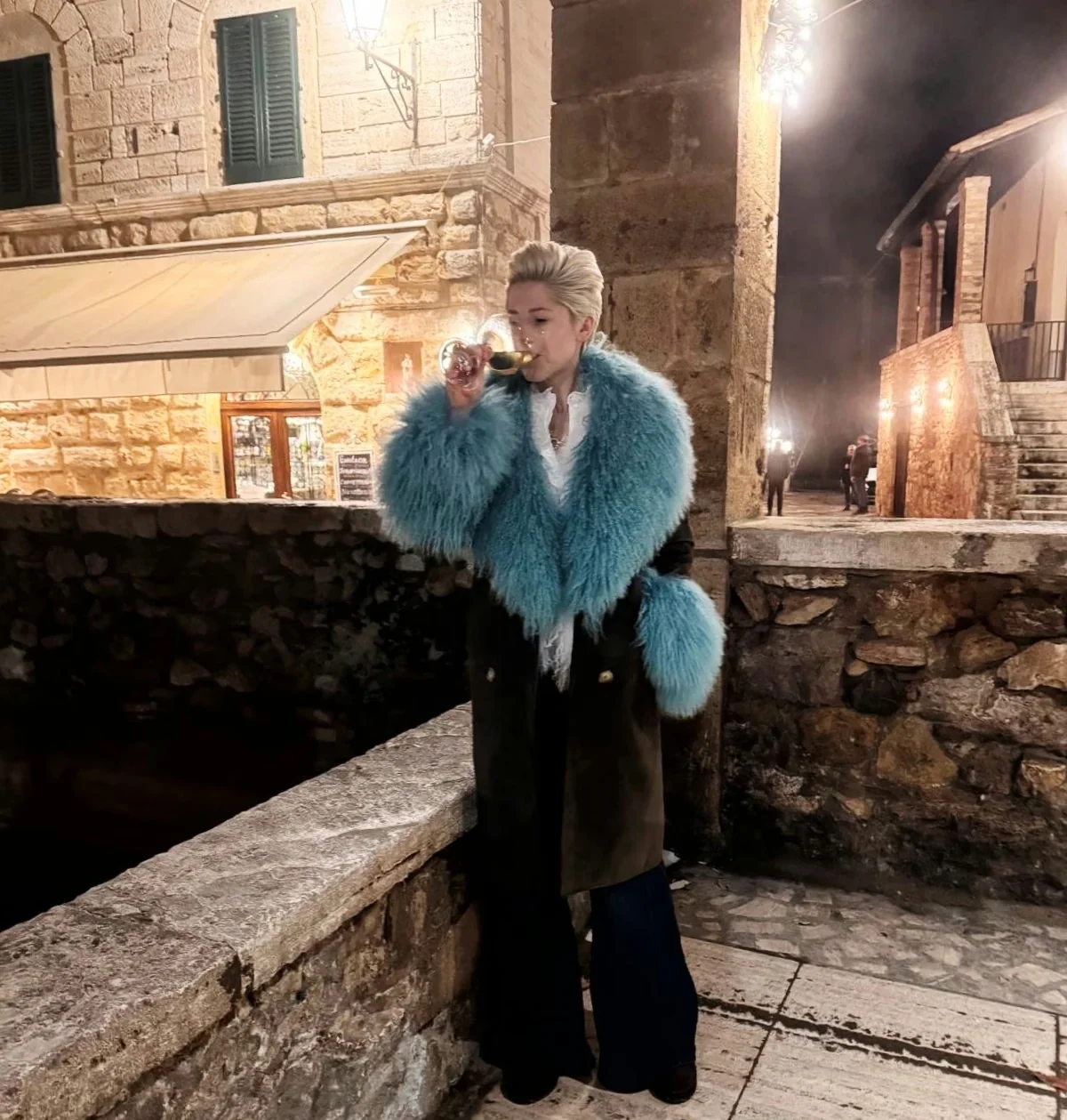 Person drinking wine in a stone-lit street at night
