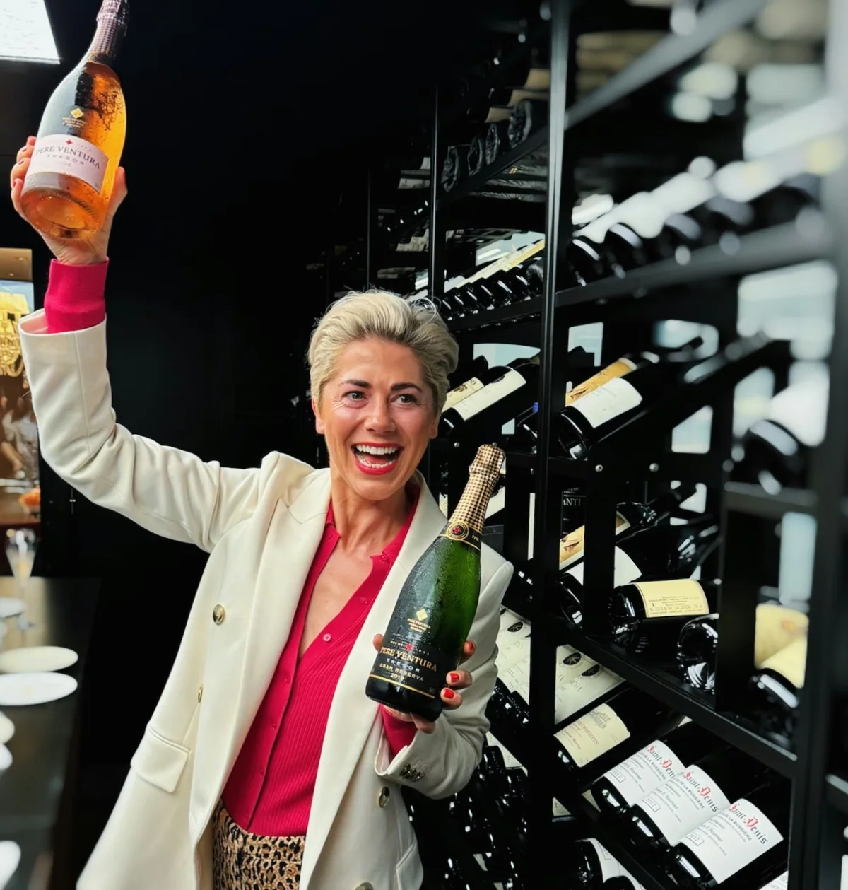 Smiling woman holding two Pere Ventura bottles beside a wine rack