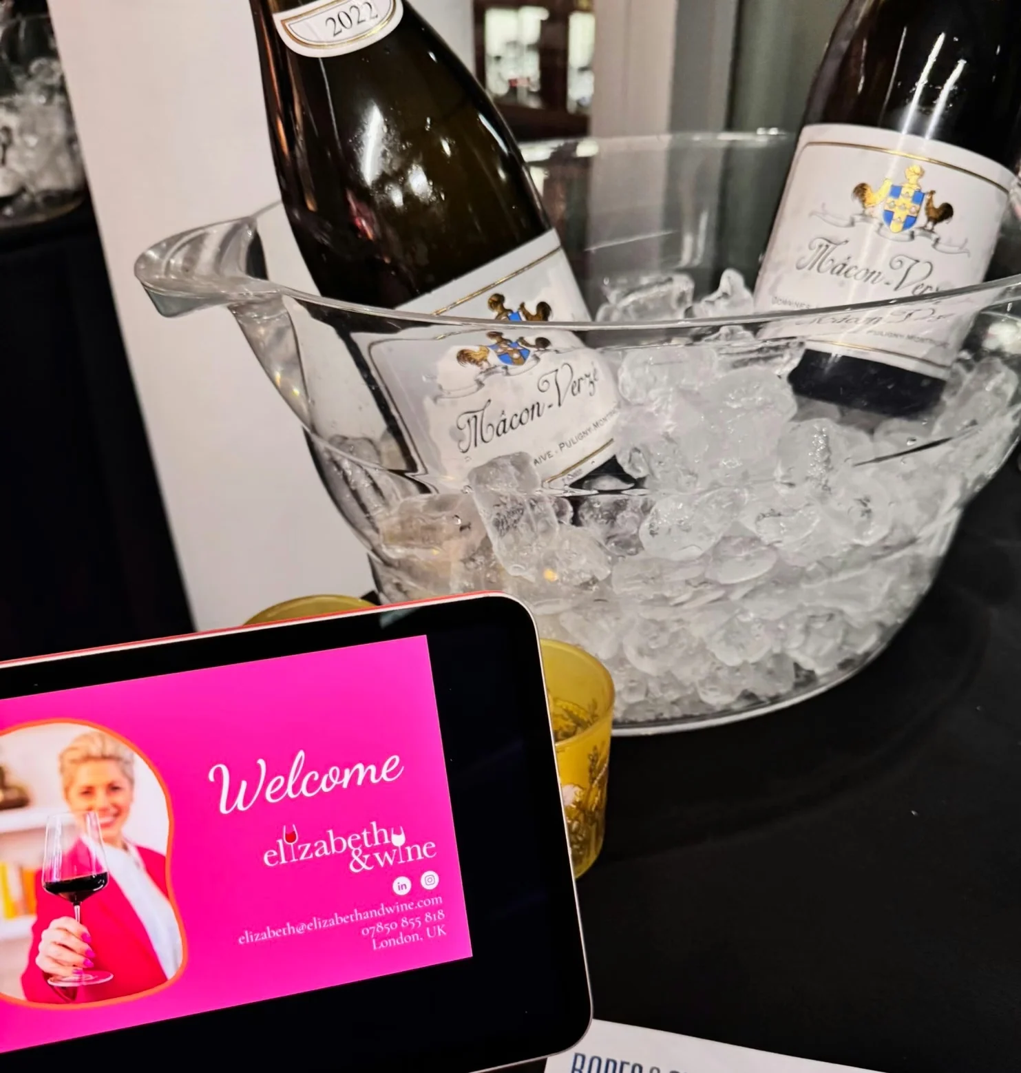 Wine bottles chilling in an ice bucket beside an Elizabeth & Wine welcome screen at a private tasting.