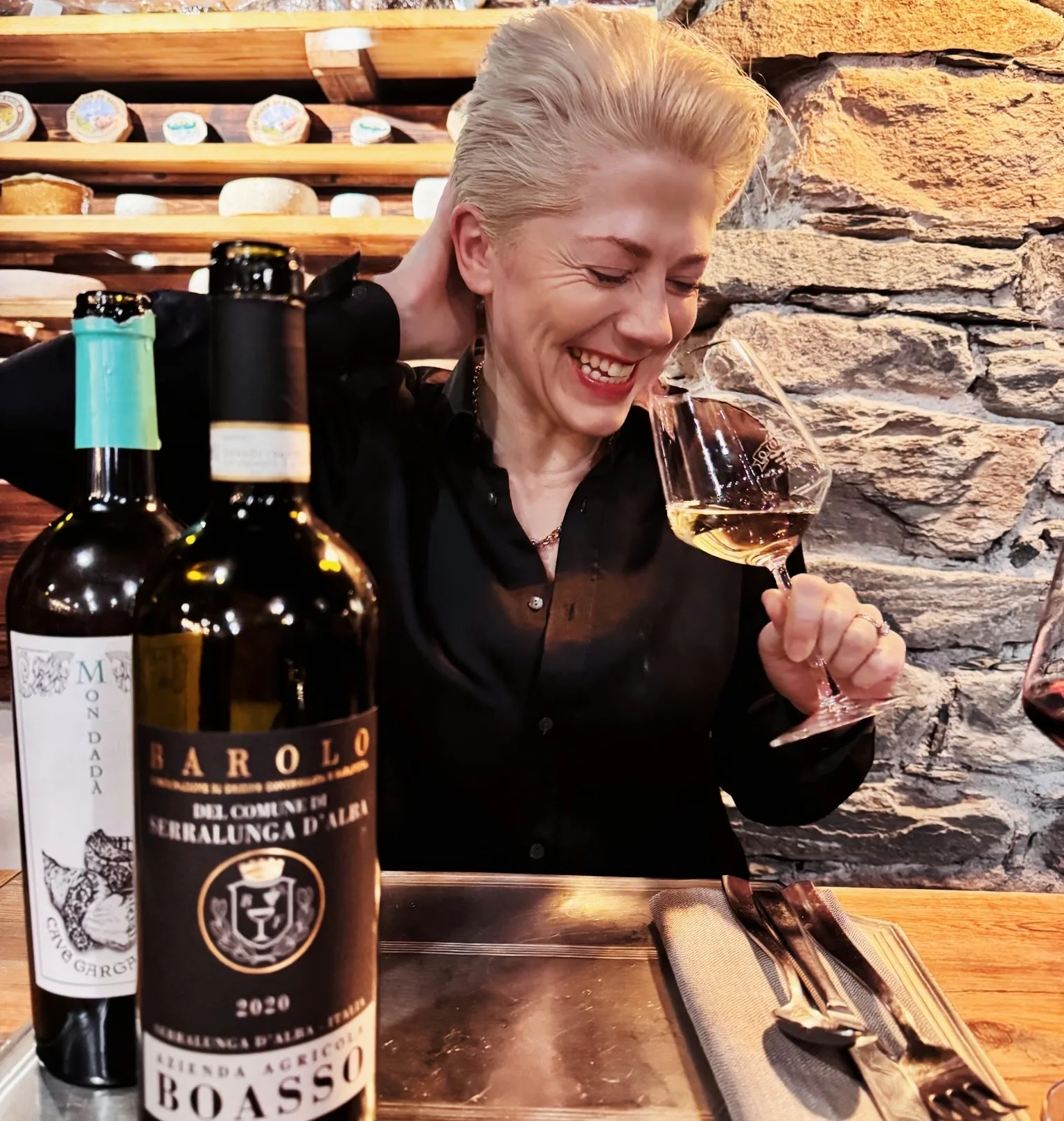 Woman holding a glass of wine beside bottles of Barolo and Monada in a rustic restaurant