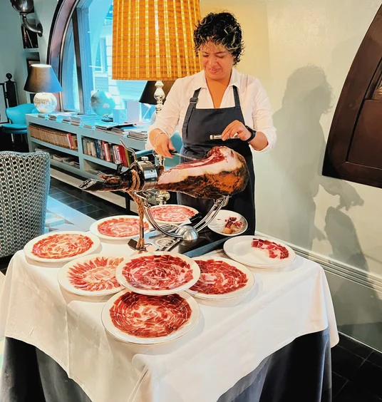Chef carving a cured ham beside plates of thinly sliced meat