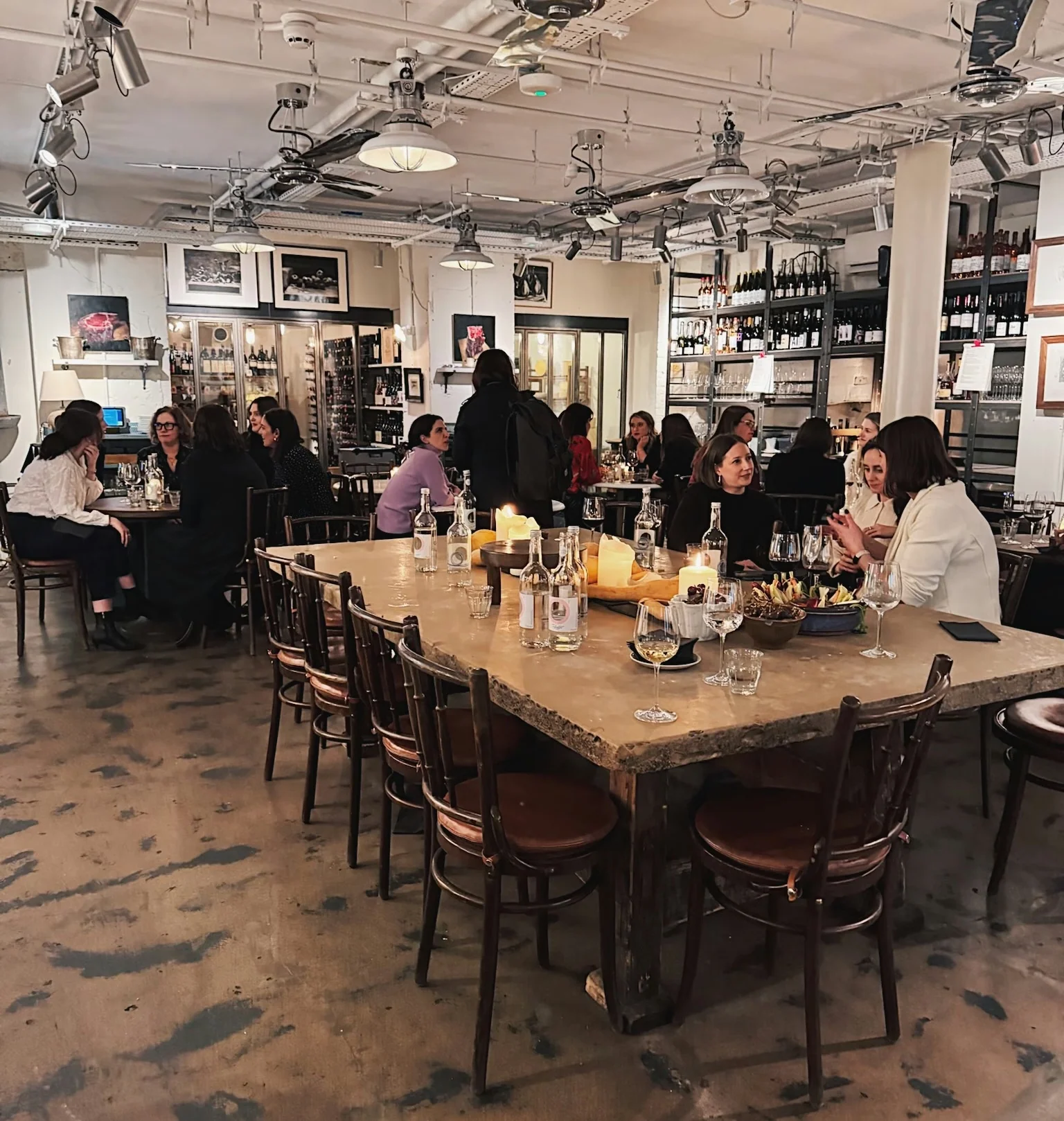 Guests enjoy wine and food at tables in a lively indoor tasting venue