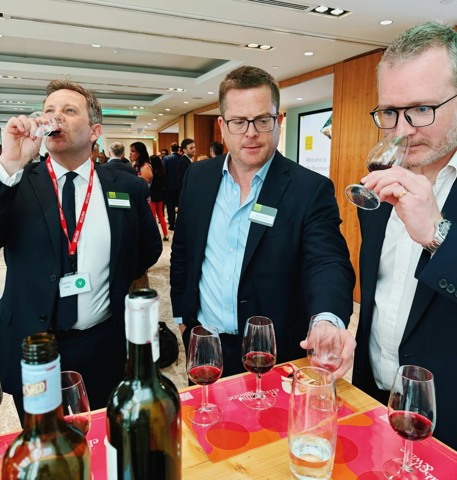 Guests taste red wine at a corporate event with wine glasses and bottles on a table