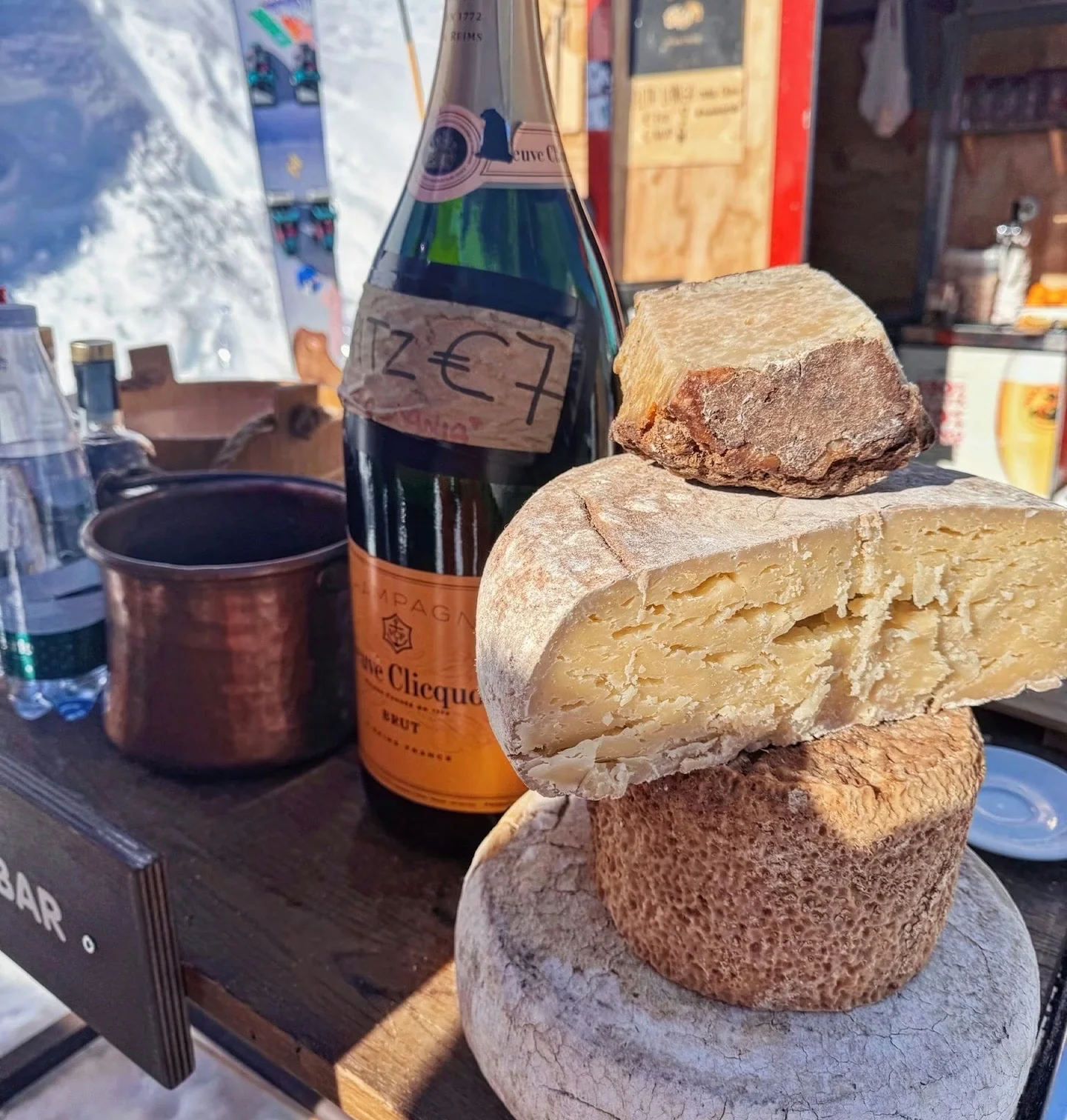 Bottle of Veuve Clicquot champagne beside stacked cheeses at an outdoor mountain bar