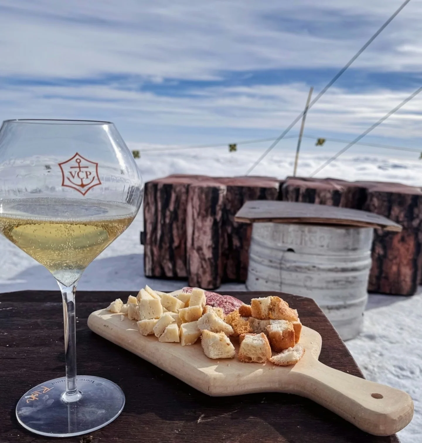 Glass of sparkling wine and a wooden board of cheese and bread on a snowy mountain terrace