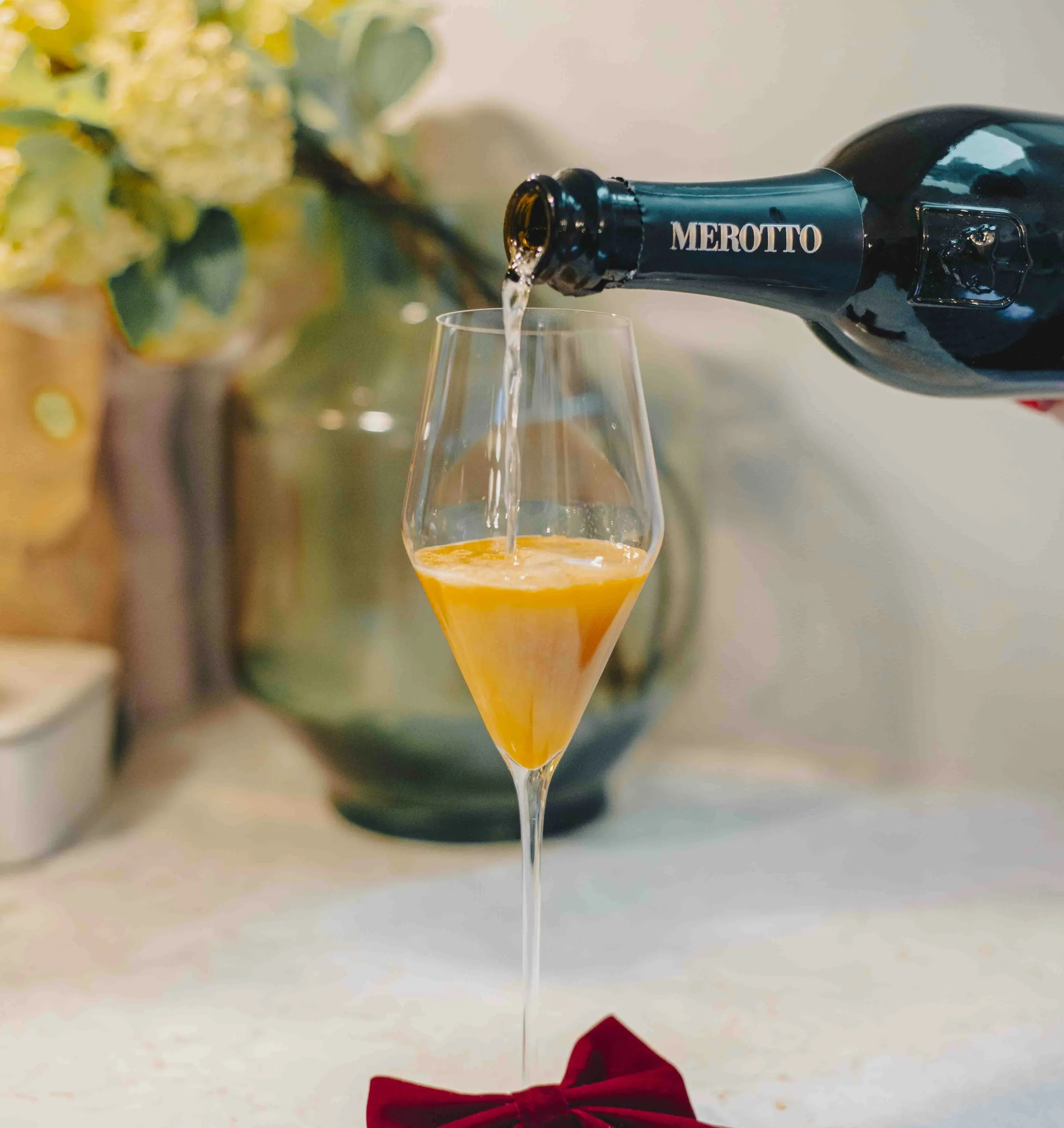 Prosecco poured into a coupe glass filled with orange cocktail and decorated with a red velvet bow