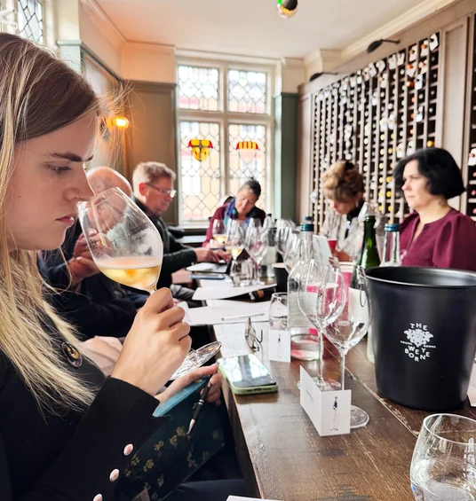 Guests taste wine around a table in a room lined with wine bottles