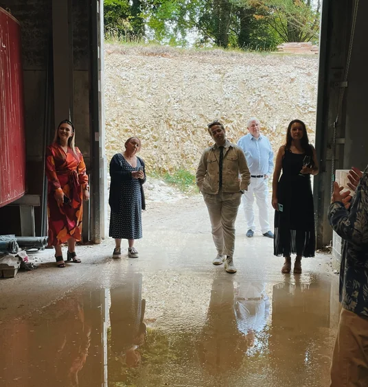 Guests gather in a winery doorway beside a pale flint wall and puddled concrete floor