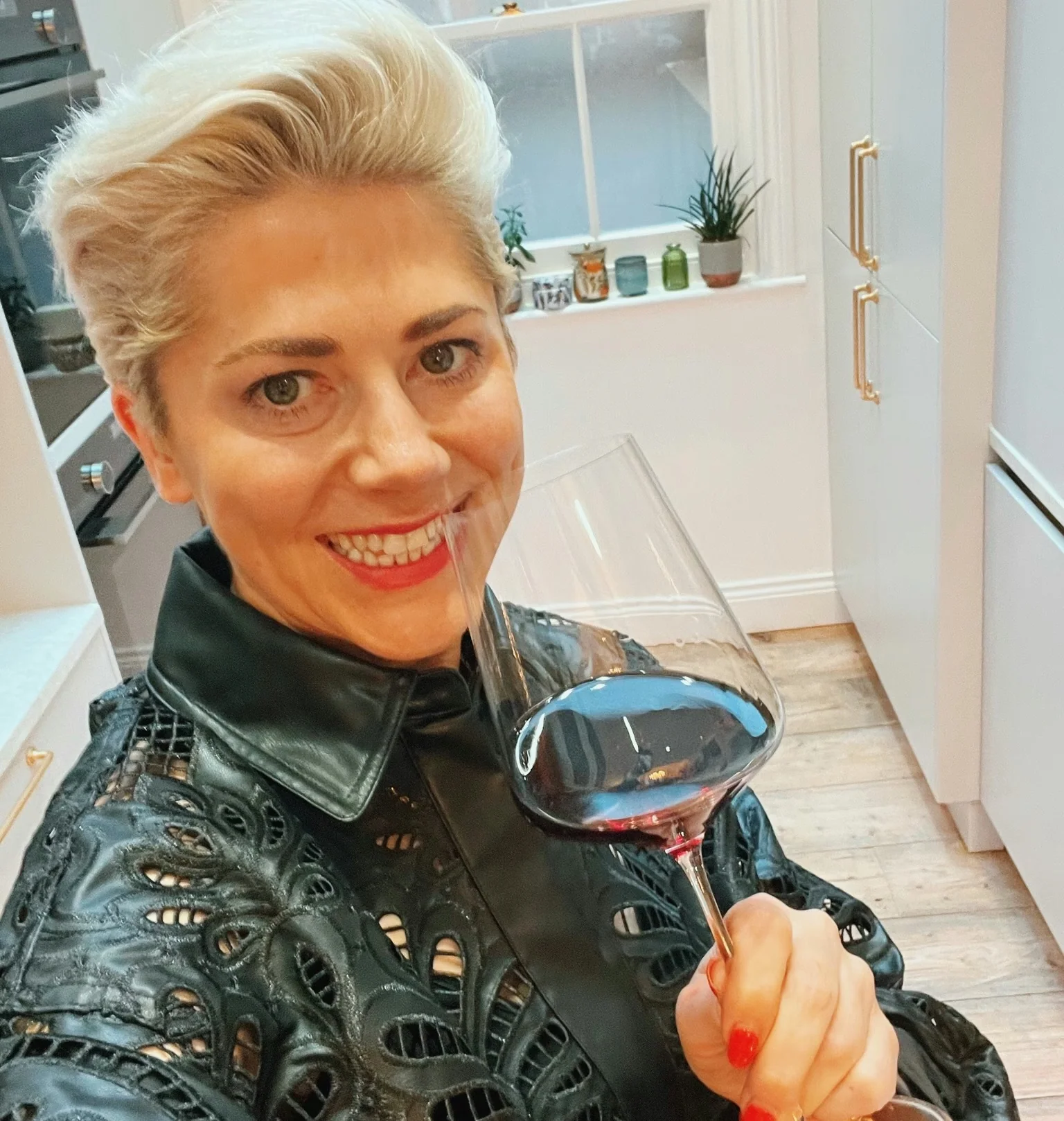 Smiling woman holding a glass of red wine in a bright kitchen