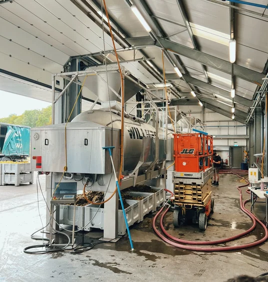 Winery interior with stainless steel tanks, equipment, hoses and a worker beside a red lift