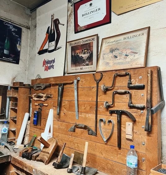 Vintage Bollinger Champagne posters displayed above a traditional workshop bench and hand tools