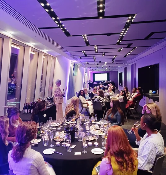 Corporate wine tasting with guests seated around a table in a purple-lit event room