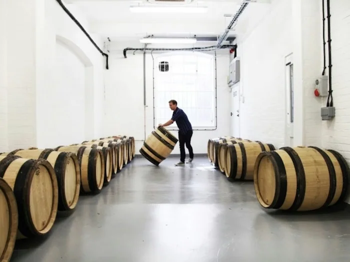 Man rolling oak wine barrel in cellar warehouse
