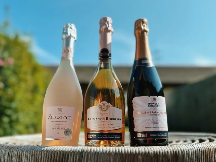 Three sparkling wine bottles on an outdoor table in sunlight