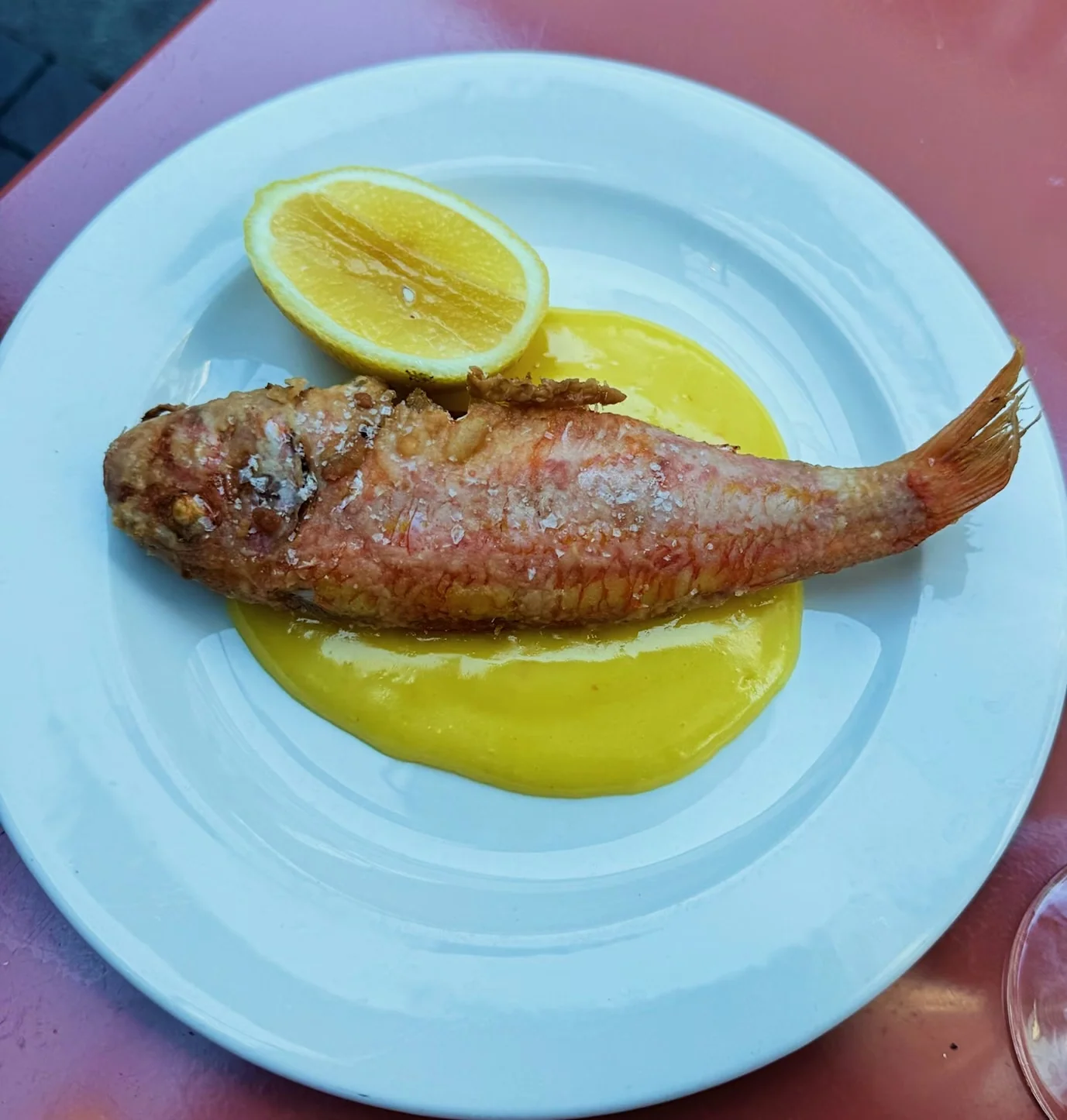 Whole cooked fish served with lemon and yellow sauce on a white plate