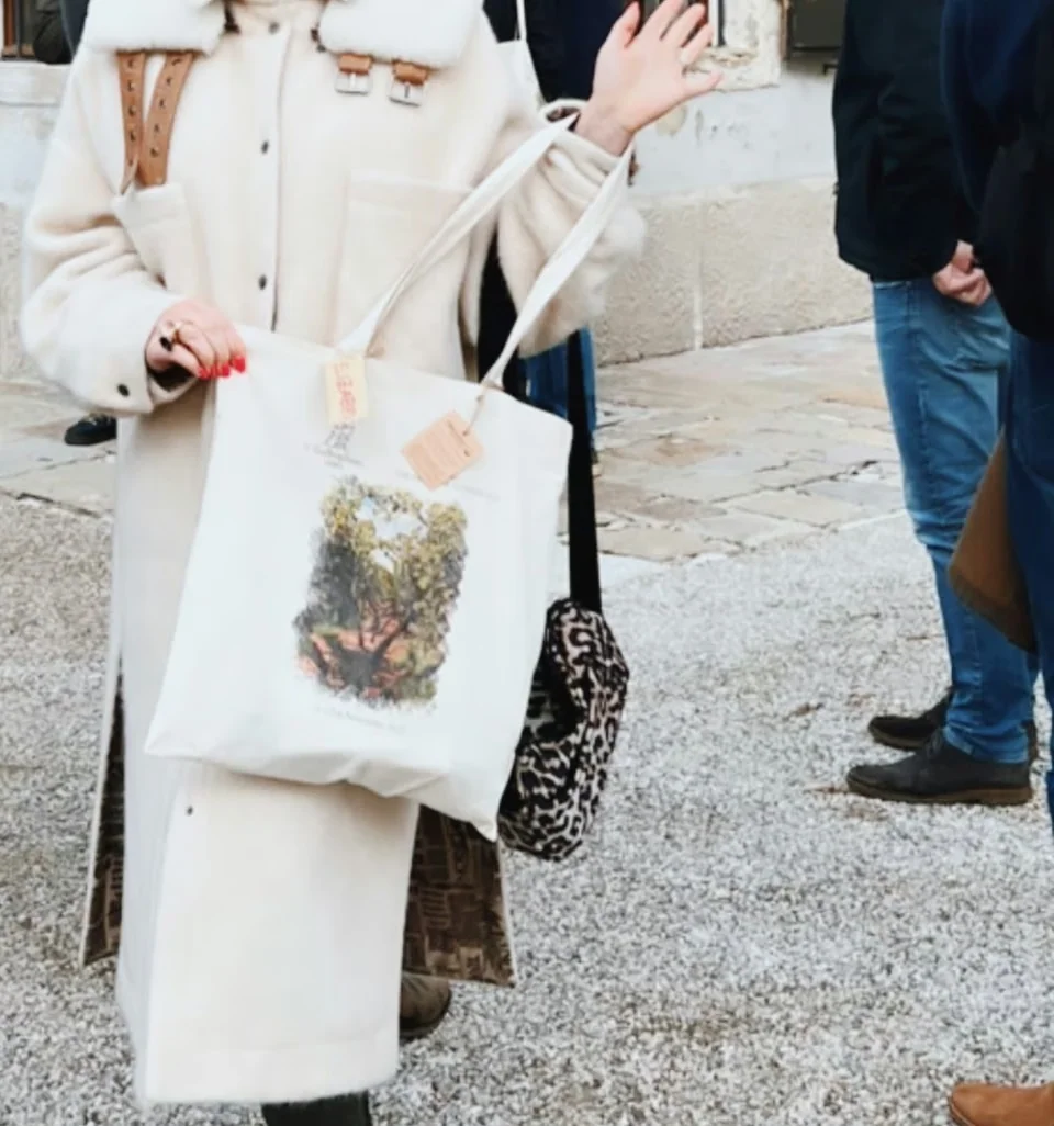 Smiling woman in a white coat and trainers gestures outside a historic building during an old vines wine conference
