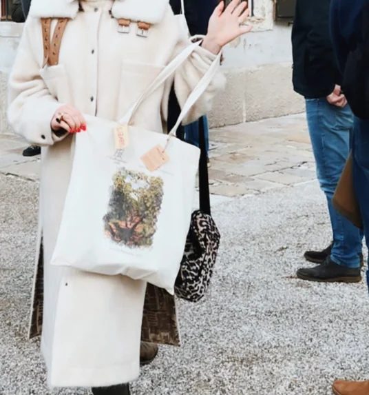 Smiling woman in a white coat and trainers gestures outside a historic building during an old vines wine conference