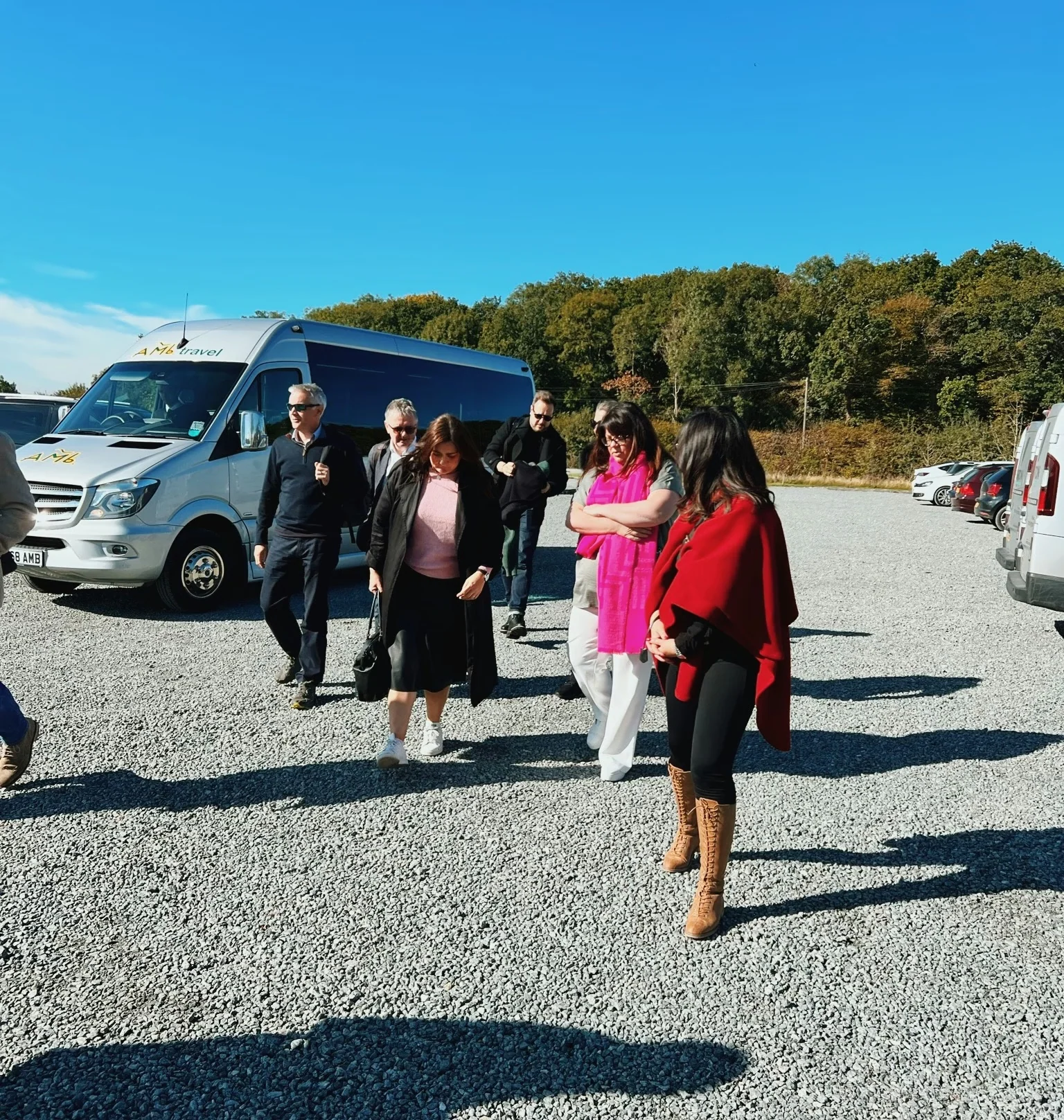 A group of visitors walks across a gravel car park beside a minibus at an English vineyard.