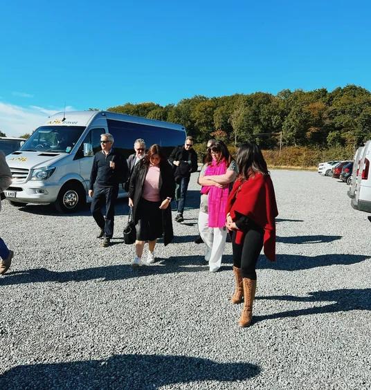 A group of visitors walks across a gravel car park beside a minibus at an English vineyard.