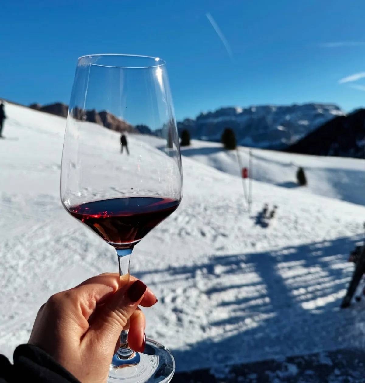 Glass of red wine held over a snowy ski slope with mountains in the background