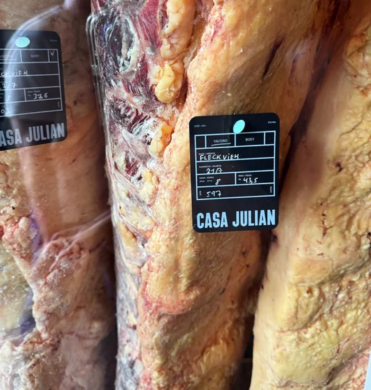 Large dry-aged beef cuts hanging with black Casa Julián labels