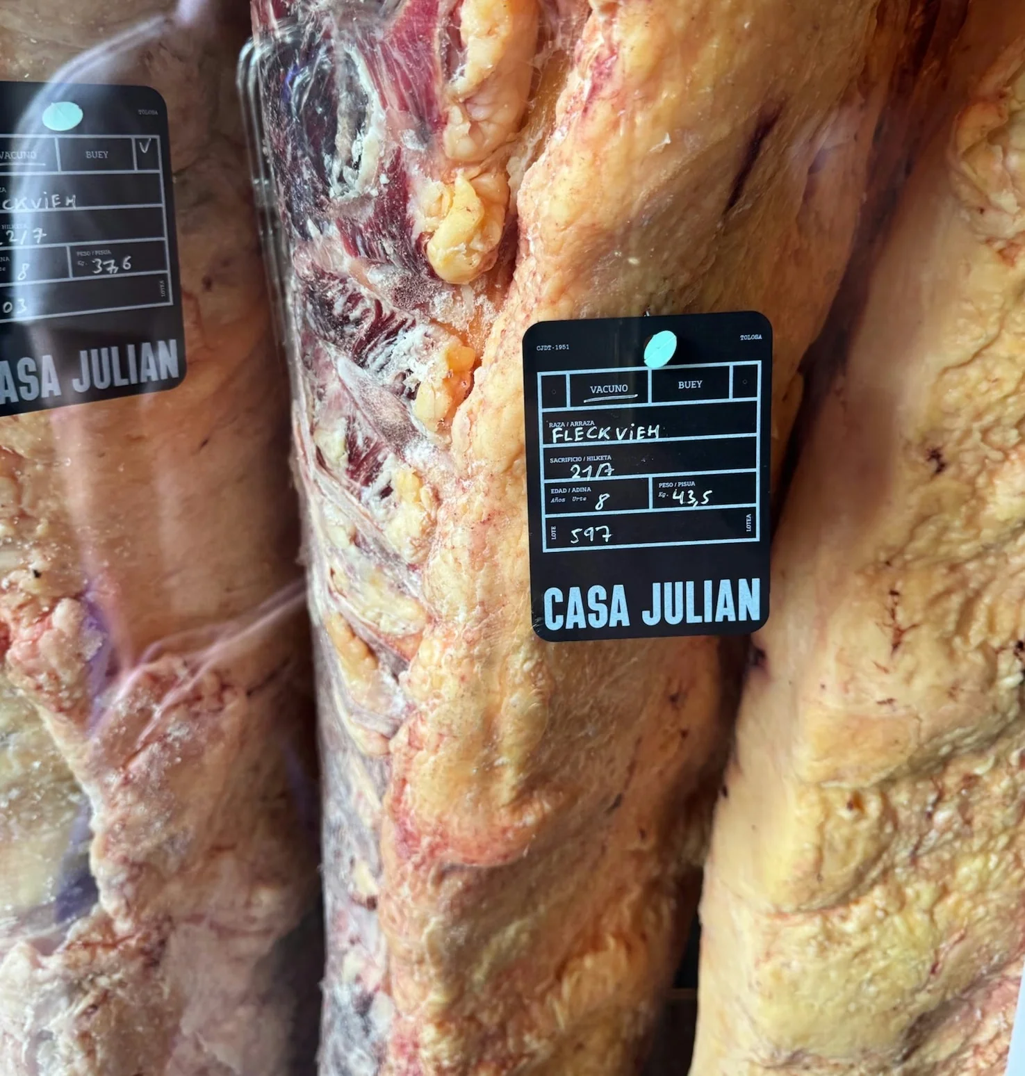 Large dry-aged beef cuts hanging with black Casa Julián labels