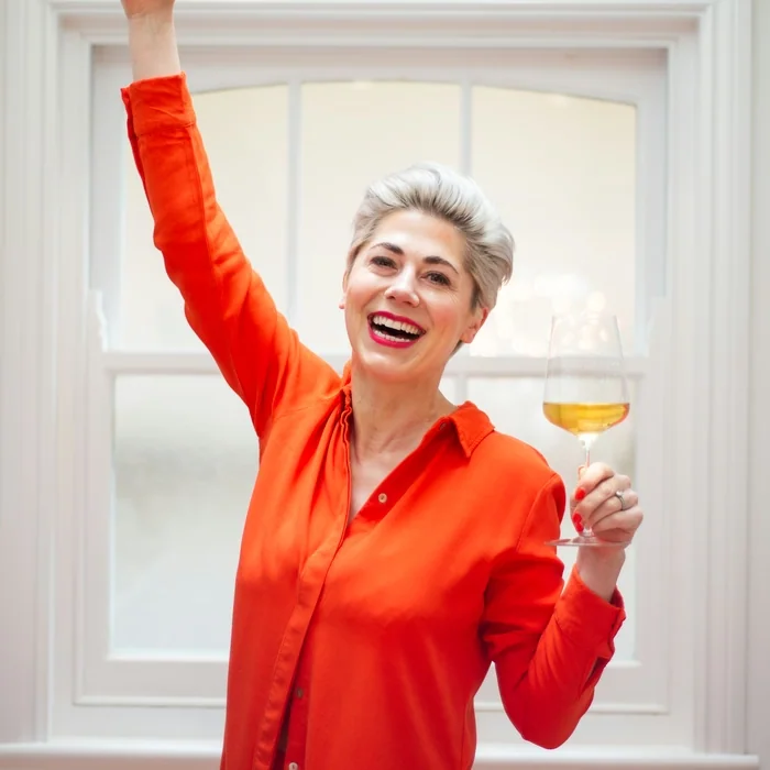 Smiling woman in red shirt holding white wine glass and raising arm