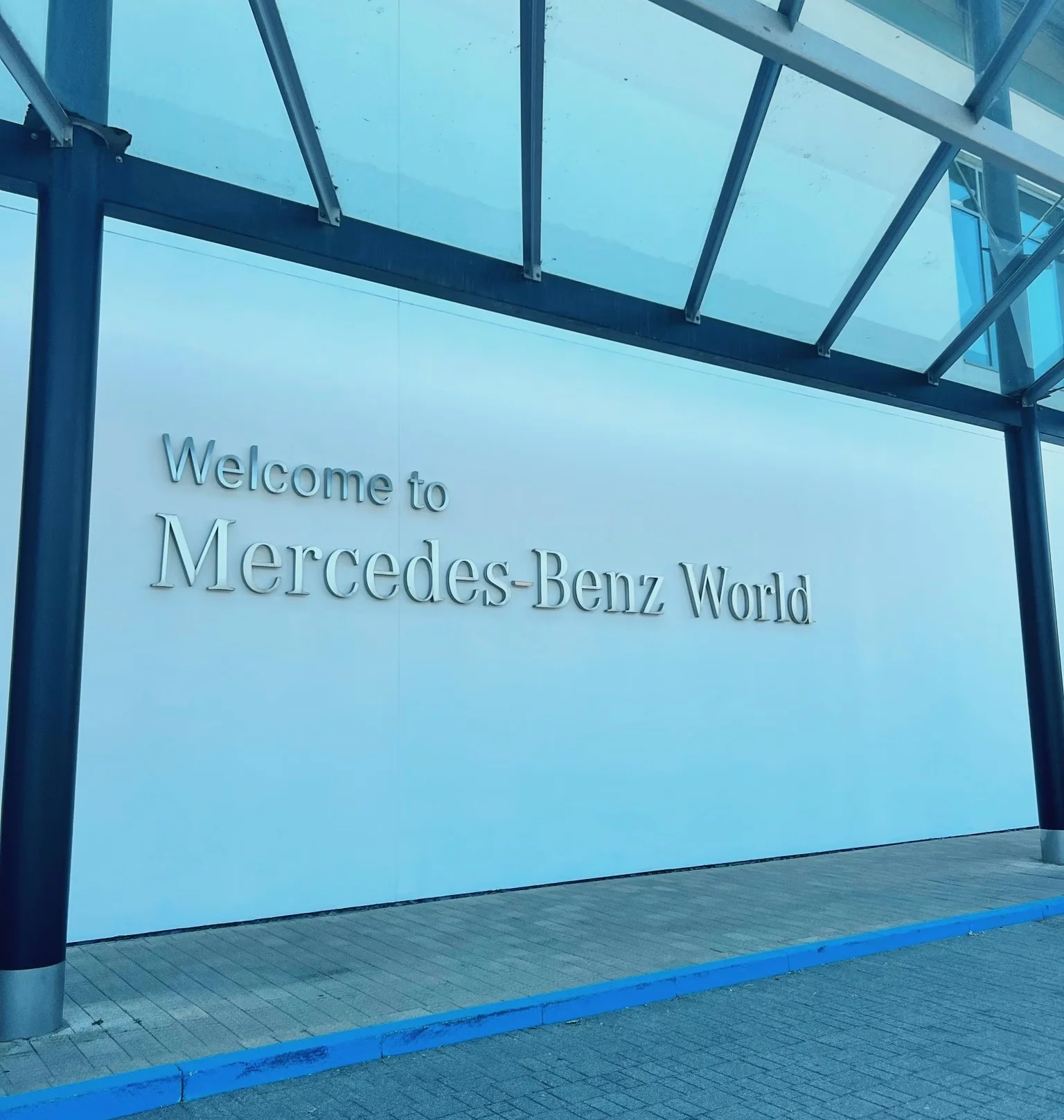 Welcome to Mercedes-Benz World sign beneath a glass canopy