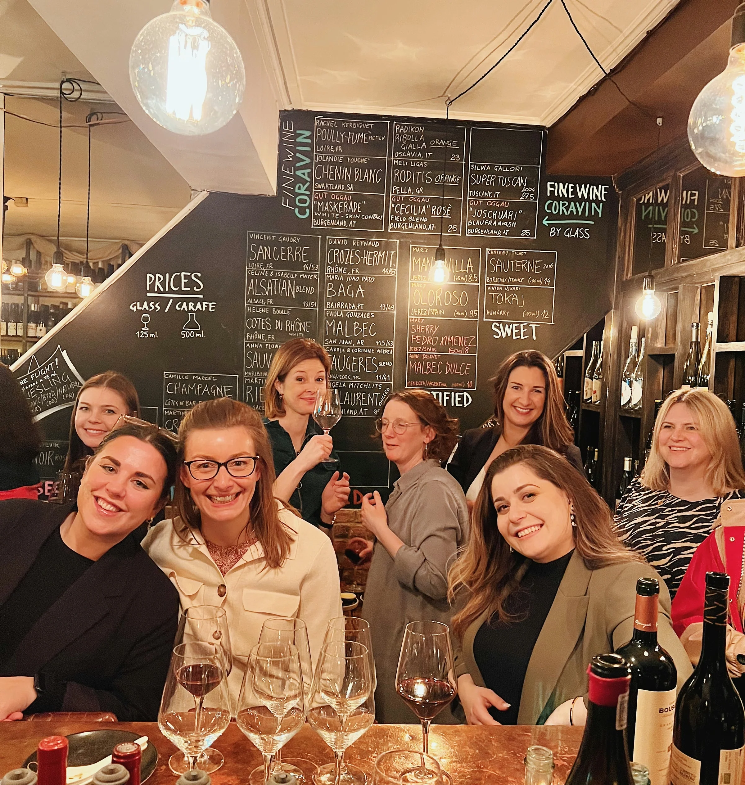 Group of women tasting wine at a restaurant bar, with wine glasses and bottles on the table