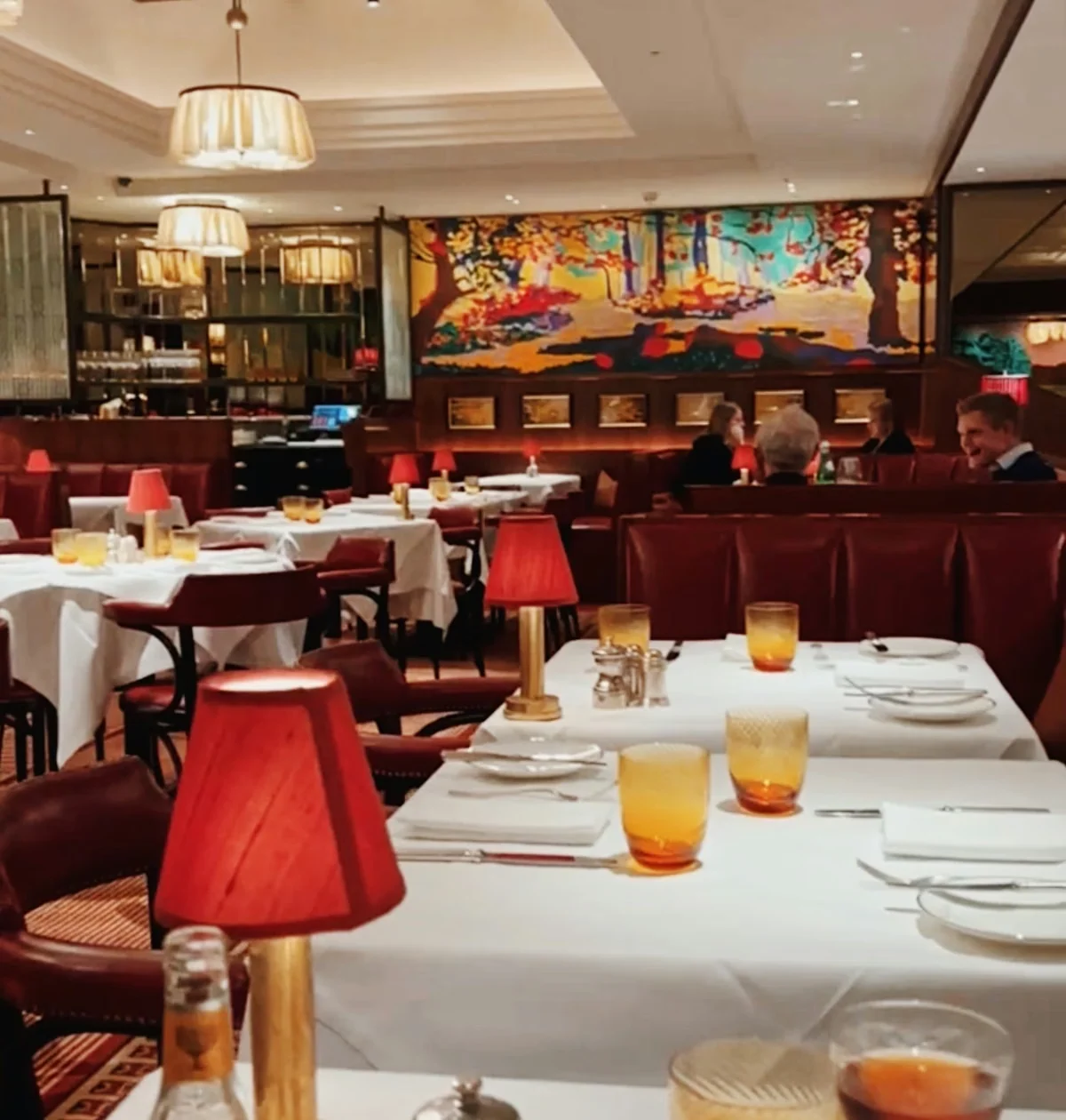 Elegant restaurant dining room with white tablecloths, red lamps, colourful artwork and seated diners