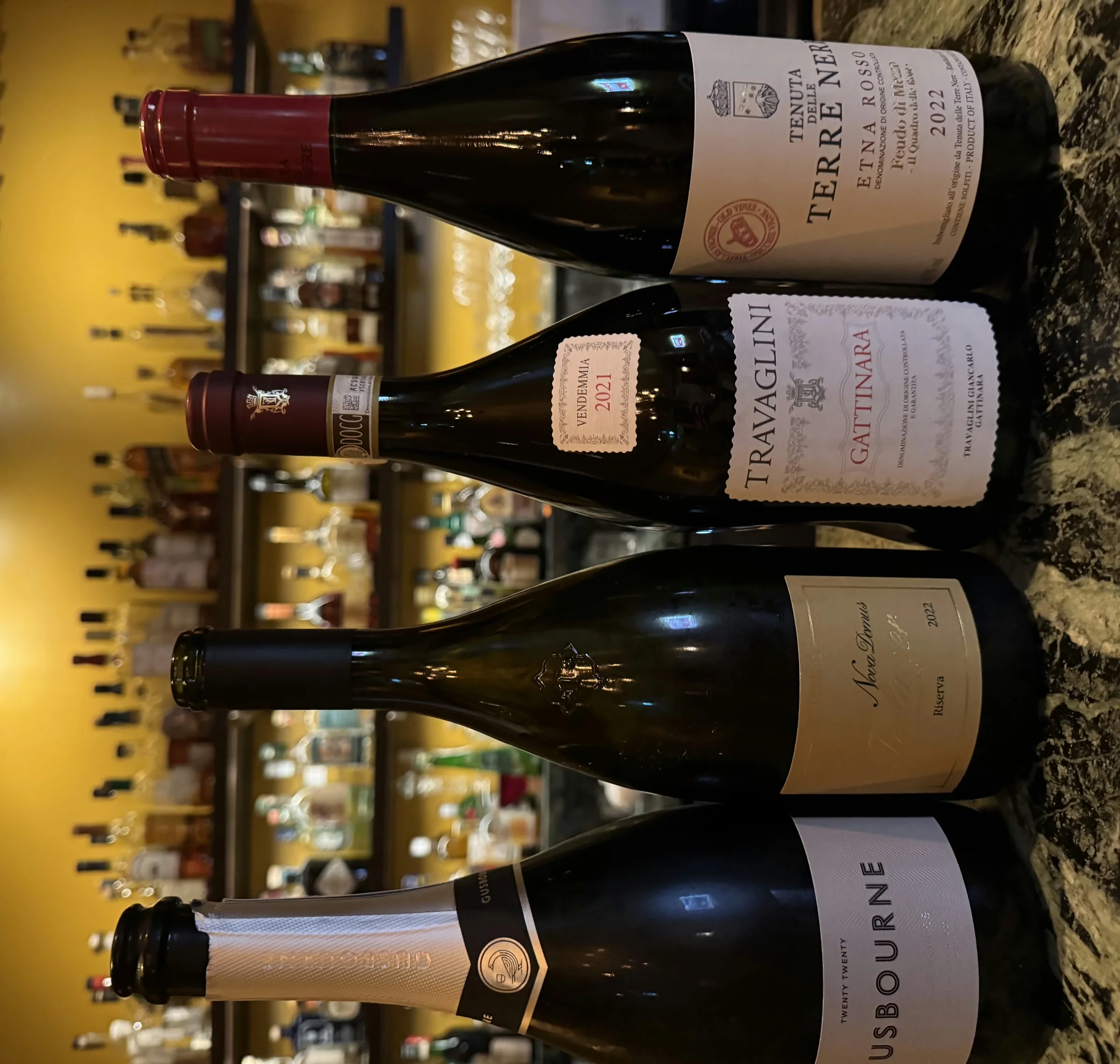 Four wine bottles, including Travaglini Gattinara and Usborne, displayed on a marble bar.