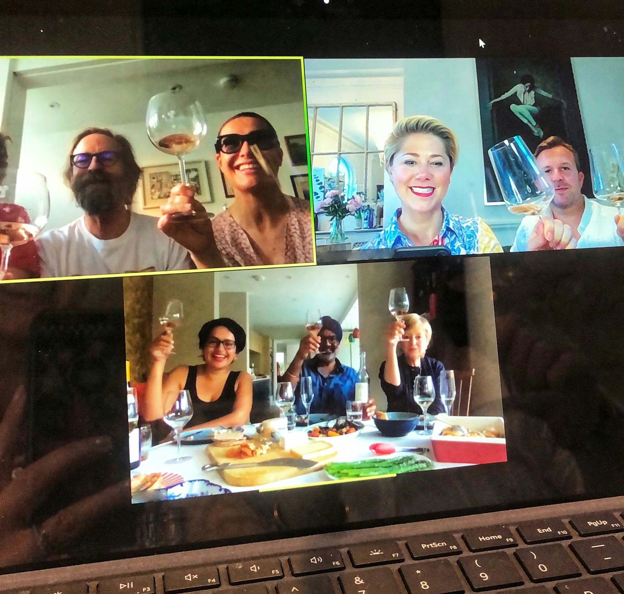 A laptop displays a virtual wine tasting, with participants raising wine glasses from their homes.